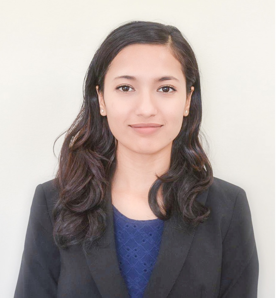 Portrait of Prabisha Shrestha. Prabisha has long wavy dark hair and is wearing a navy blouse under a dark gray suit jacket. She is looking at the camera.