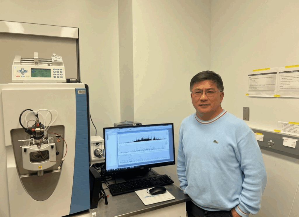 Dr. Xian Chen next to a mass spectrometry machine