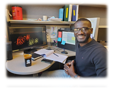 A diverse scienitst named Uriel Jean-Baptiste sits at desk in the Neher lab