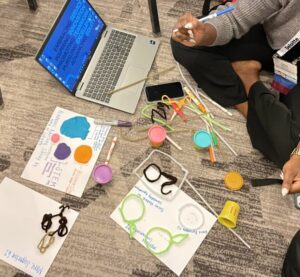 An overhead view of a person sitting on the floor with an open laptop. They are using pipe cleaners and other small materials to build a data visualization.