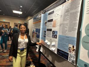 A Black woman points to her research poster.