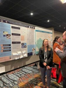 A white woman presents her research poster to a white man.