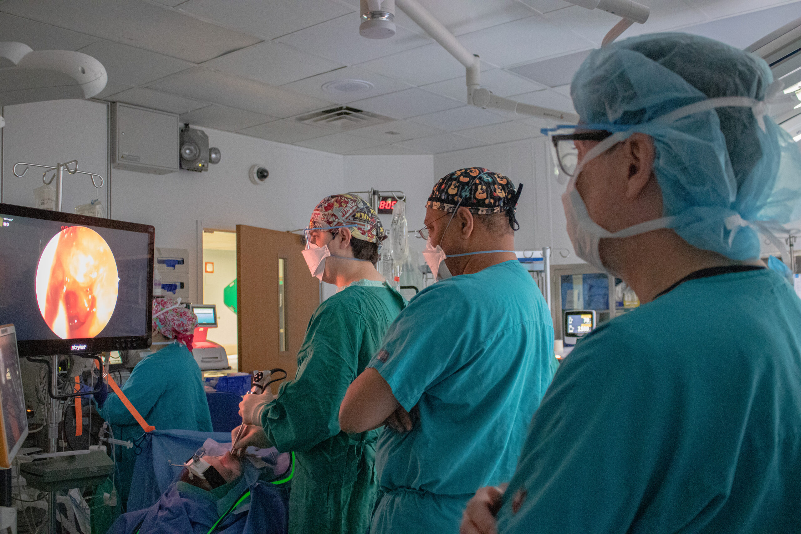 three doctors in the OR dressed in scrubs looking at a screen with the visual from the endoscope in the patients nose