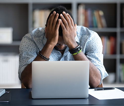 A man working at his computer, has his hands in his head, looking overwhelmed.