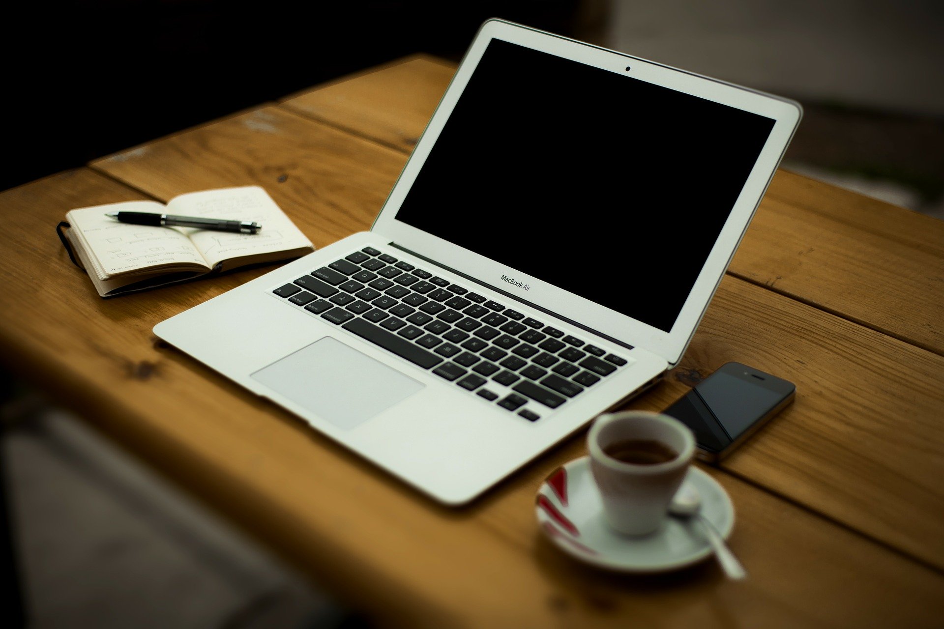 Open laptop on a desk with cup of coffee and a notepad with pen