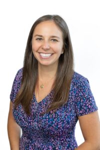 Megan Wattsm Woman with long brown hair wearing a purple and blue dress