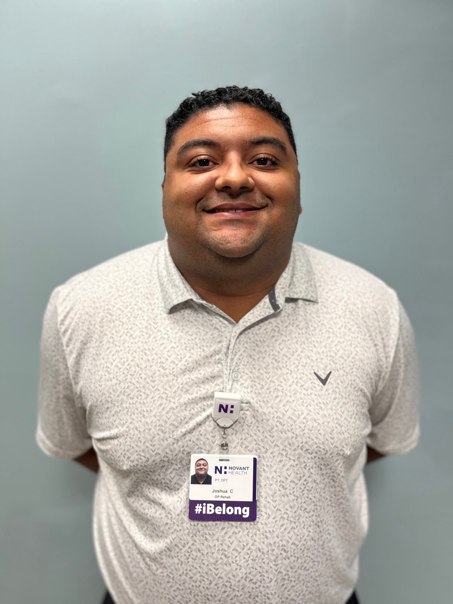 Joshua Copeland standing in front of a blank, grey wall and smiling.
