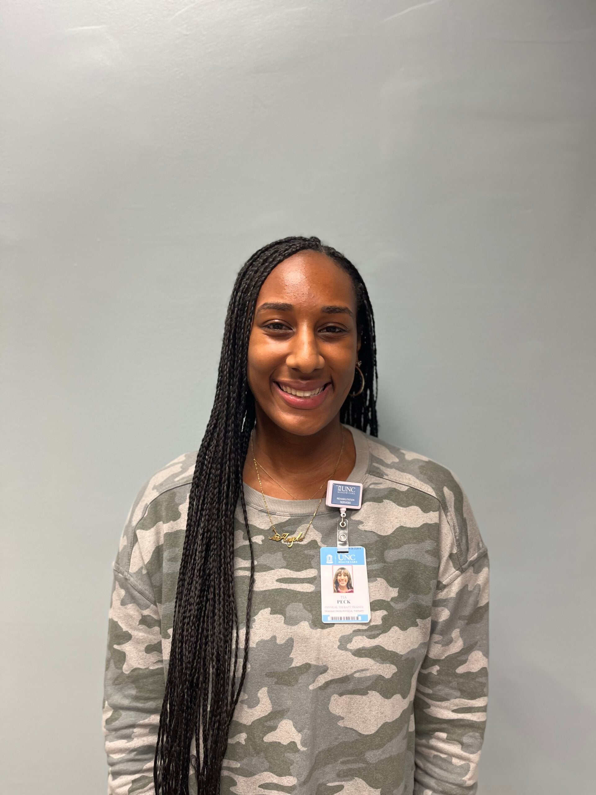 Tia Peck in a camo long-sleeve shirt smiling in front of a grey background.