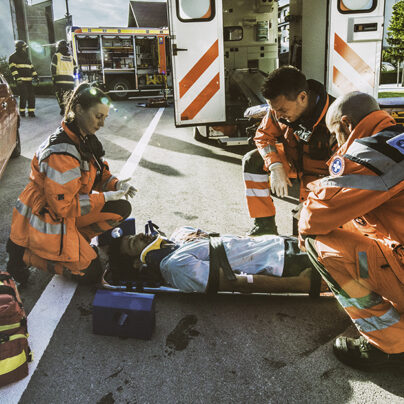 Three paramedics prepare to lift a car accident survivors into an ambulance using a stretcher.