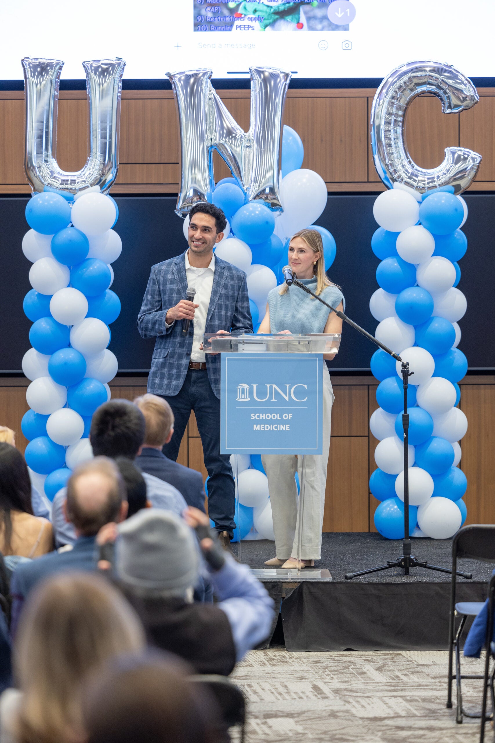 Yasine Mirmozaffari and Mia Hodges stand on a stage as the student emcees for UNC School of Medicine's 2025 Match Day.