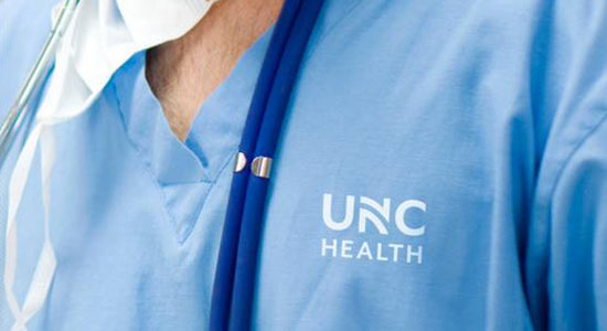 doctor wearing blue scrubs with the UNC Health logo visible.