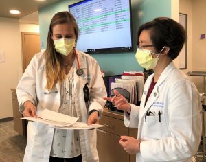 two physicians compare printed medical notes on a sheet of paper