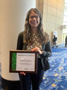 Dr. Monica Diaz holds an American Academy of Neurology Health Equity Award plaque inside a conference venue.