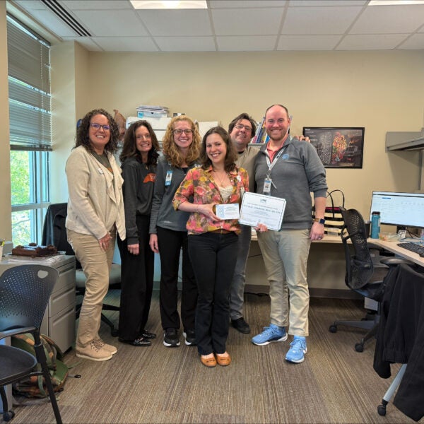 UNC Neurology dietitian Natalia Adamson stands with colleagues in an office setting holding award certificates.