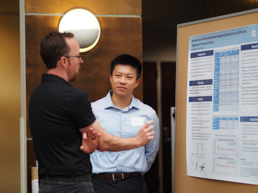 Two attendees discuss a research poster during a Neurology Day 2026 poster session in an indoor conference space.