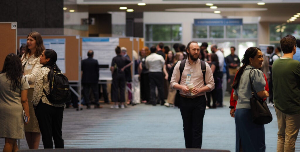 Attendees walk through a busy poster session at Neurology Day 2026, viewing research displays in a large indoor conference space.