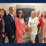 UNC Children’s leaders and staff stand together beside a wall plaque marking the opening of the new Pediatric Cardiac Intensive Care Unit (PCICU).
