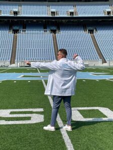 Blaide Woodburn ready to go in his Pharmacology white coat as he stands on the UNC Kenan stadium's 50 yard line.