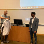 Dr. Henrik Dohlman shows the back of Dr. Lucas Aponte-Collazo's Pharmacology White Coat at his White Coat Ceremony, showing the words, "UNC Pharmacology".