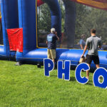 PharmFest Foosball Players outside the inflatable game area with a PHCO sign in front