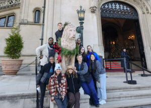 Pharmacology 2nd year students stand around a statue of a lion decorated with seasonal Christmas wreaths by a fancy light pole in front of an entrance at the Biltmore Estate in Asheville, NC.