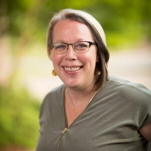 Professional head-shot of a woman with blurred outdoor background.