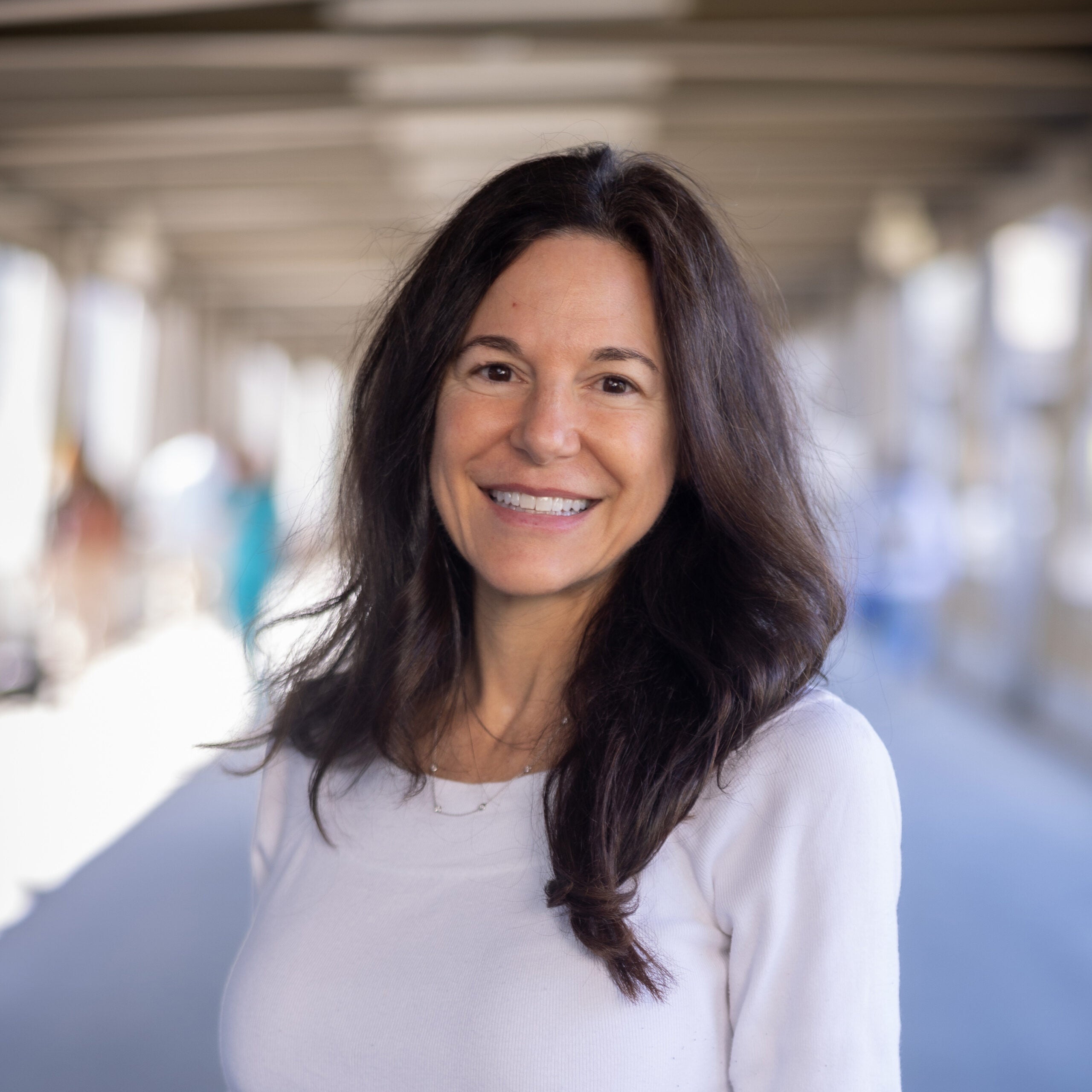Josephine "Pina" Finazzo headshot. Female with long dark brown hair and eyes is smiling at the camera. She is wearing a long-sleeve white sweater top.