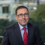 Ersan Alton headshot. Male with short dark hair and eyes wearing glasses looking at the camera. He is wearing a blue shirt, red tie, and black suit jacket.