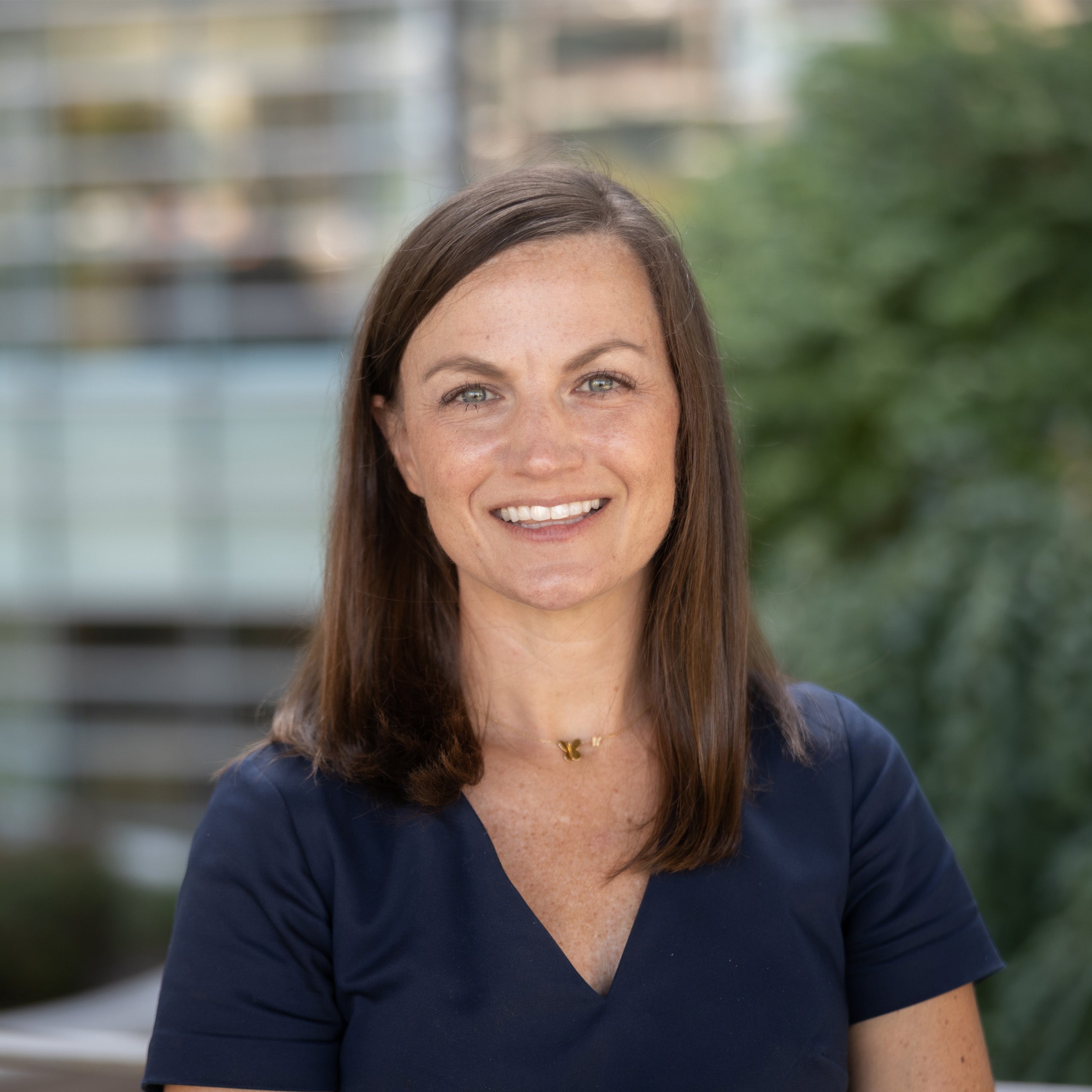 Lauren Burke's headshot. A female with shoulder-length dark brown hair and green eyes is smiling at the camera. She is wearing a navy dress.