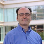 Jorge Oldan's headshot. Male with brown thinning hair and brown eyes wearing glasses. He is wearing a blue open-collar button-down shirt.