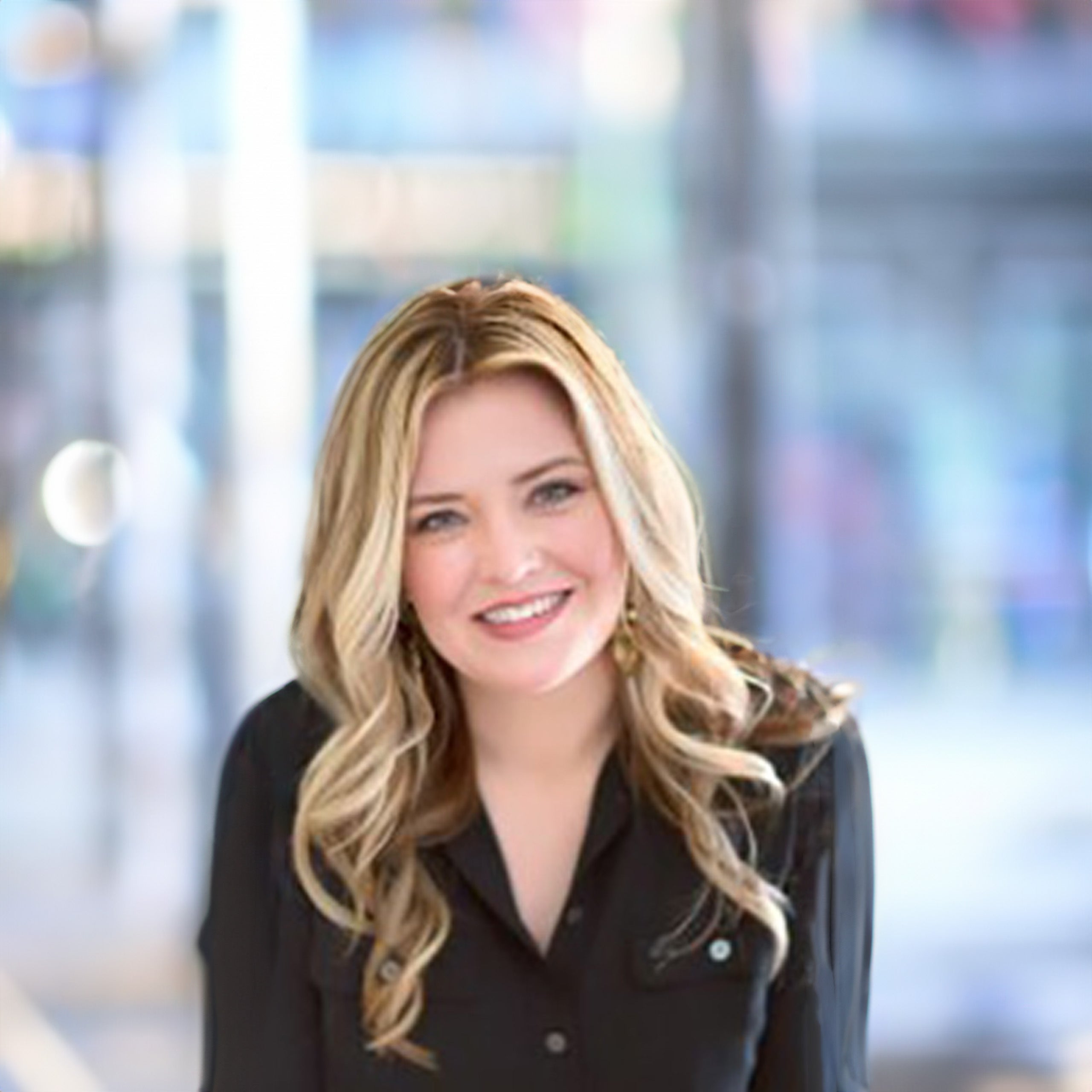 Emily Gardner headshot. Female with long blond hair and green eyes smiling at the camera. She is wearing an open-collar, long-sleeve black button-down.