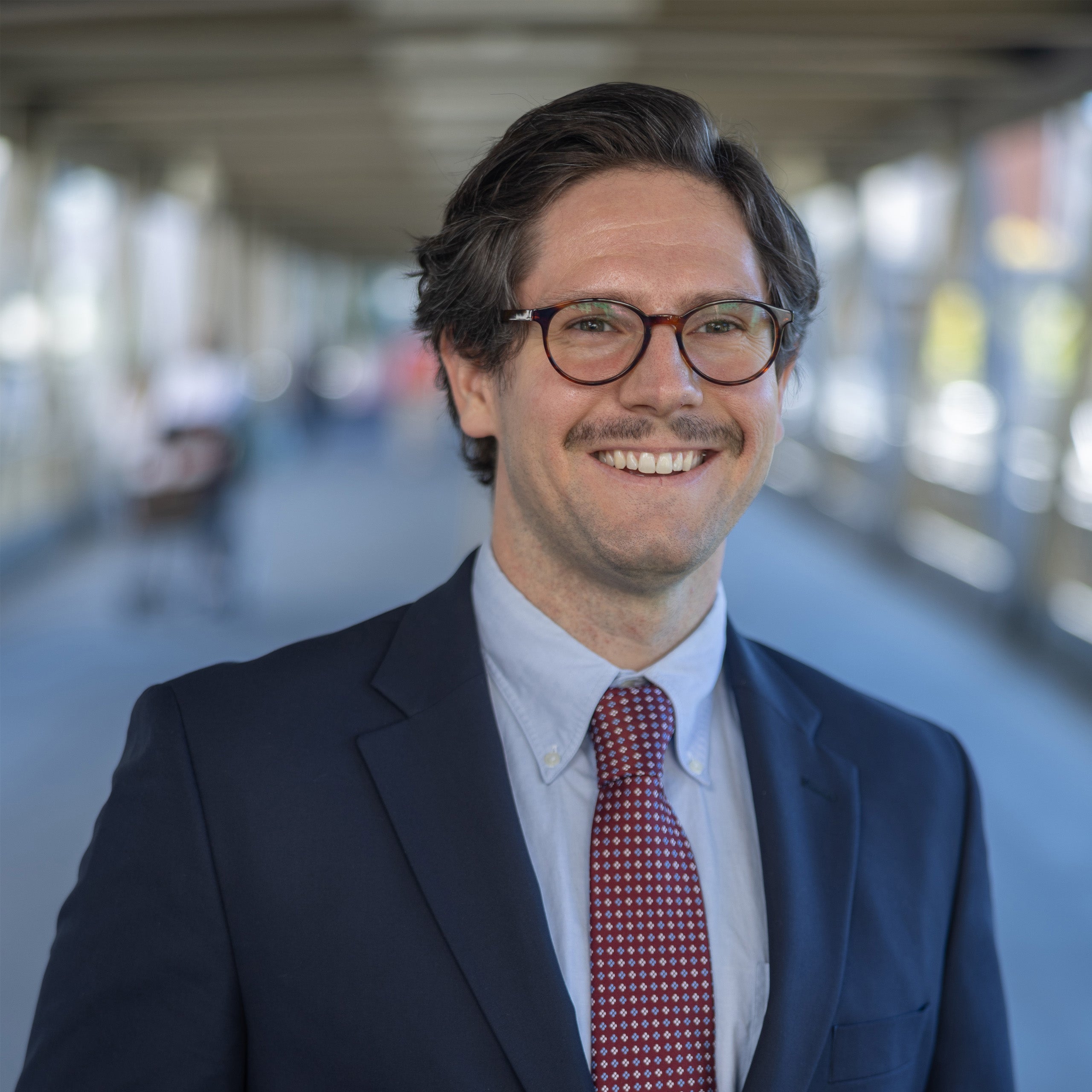 Matt Gellatly headshot. Male with brown Jair and eyes wearing glasses is smiling at the camera. He is wearing a blue shirt, red tie, and navy jacket.