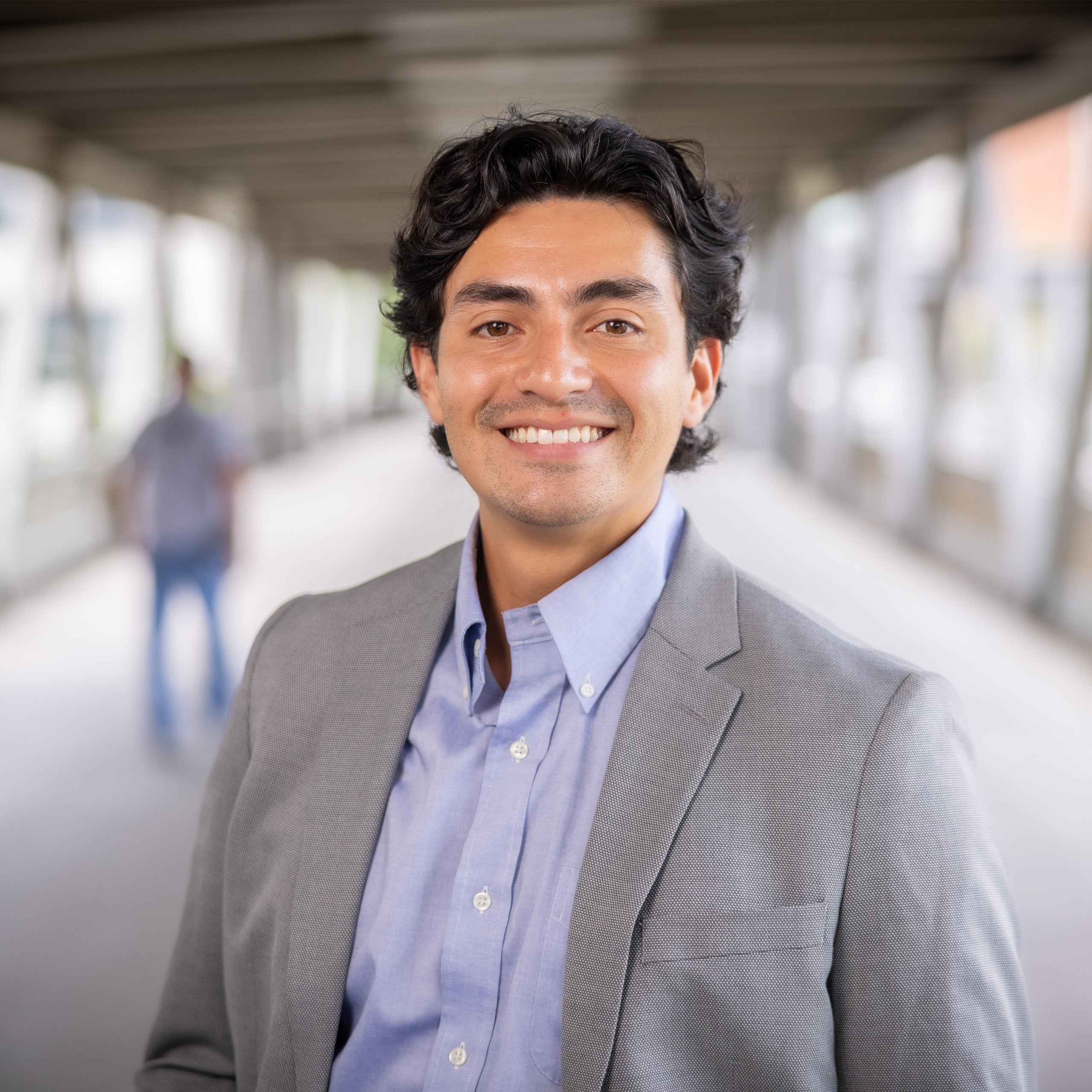 Franco Godoy headshot. Male with dark brown hair and light brown eyes smiling at the camera. He is wearing a open collard blue shirt and light grey jacket.