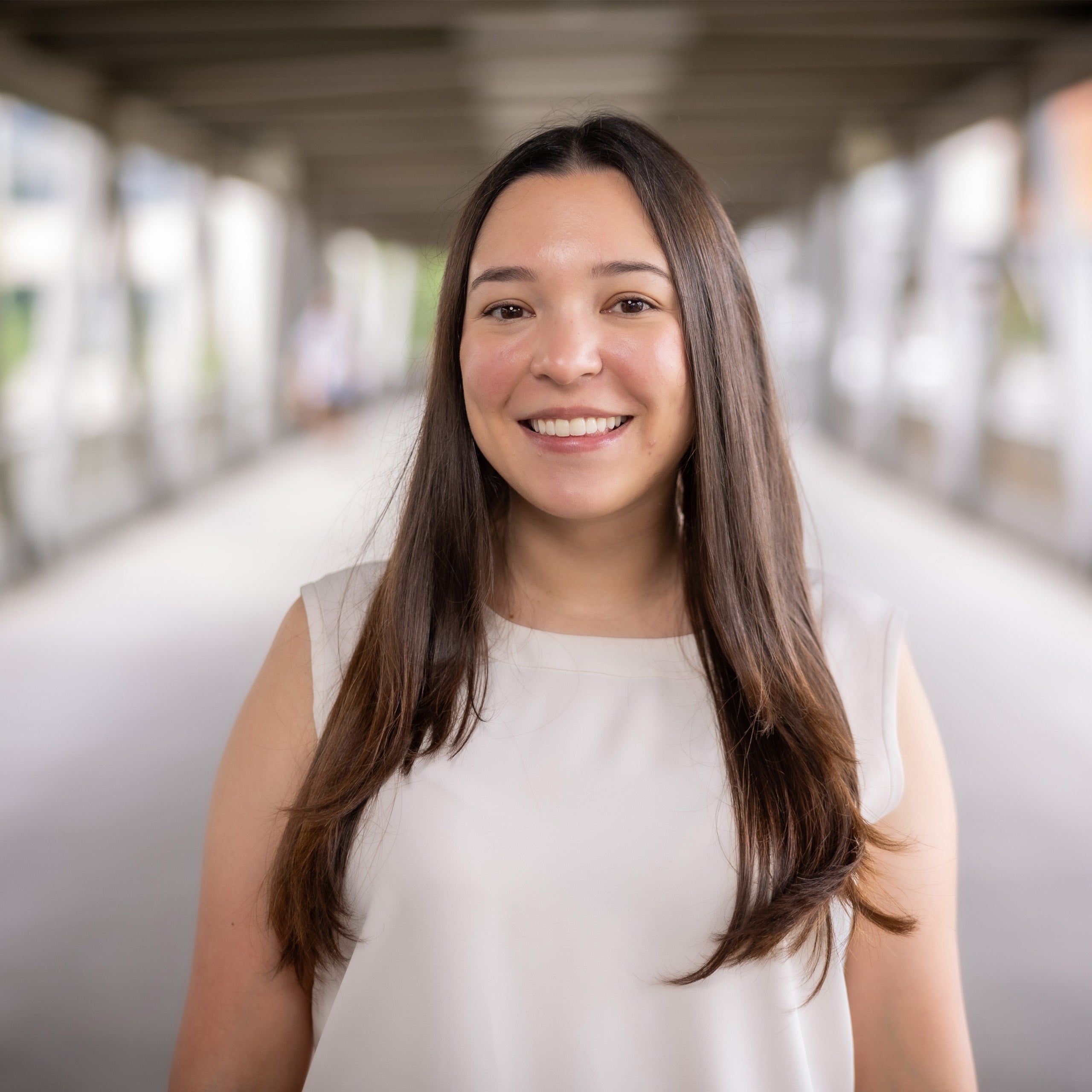 Bianca Martinez headshot. Female with long brown hair and eyes smiling at the camera. She is wearing a sleeveless white blouse.