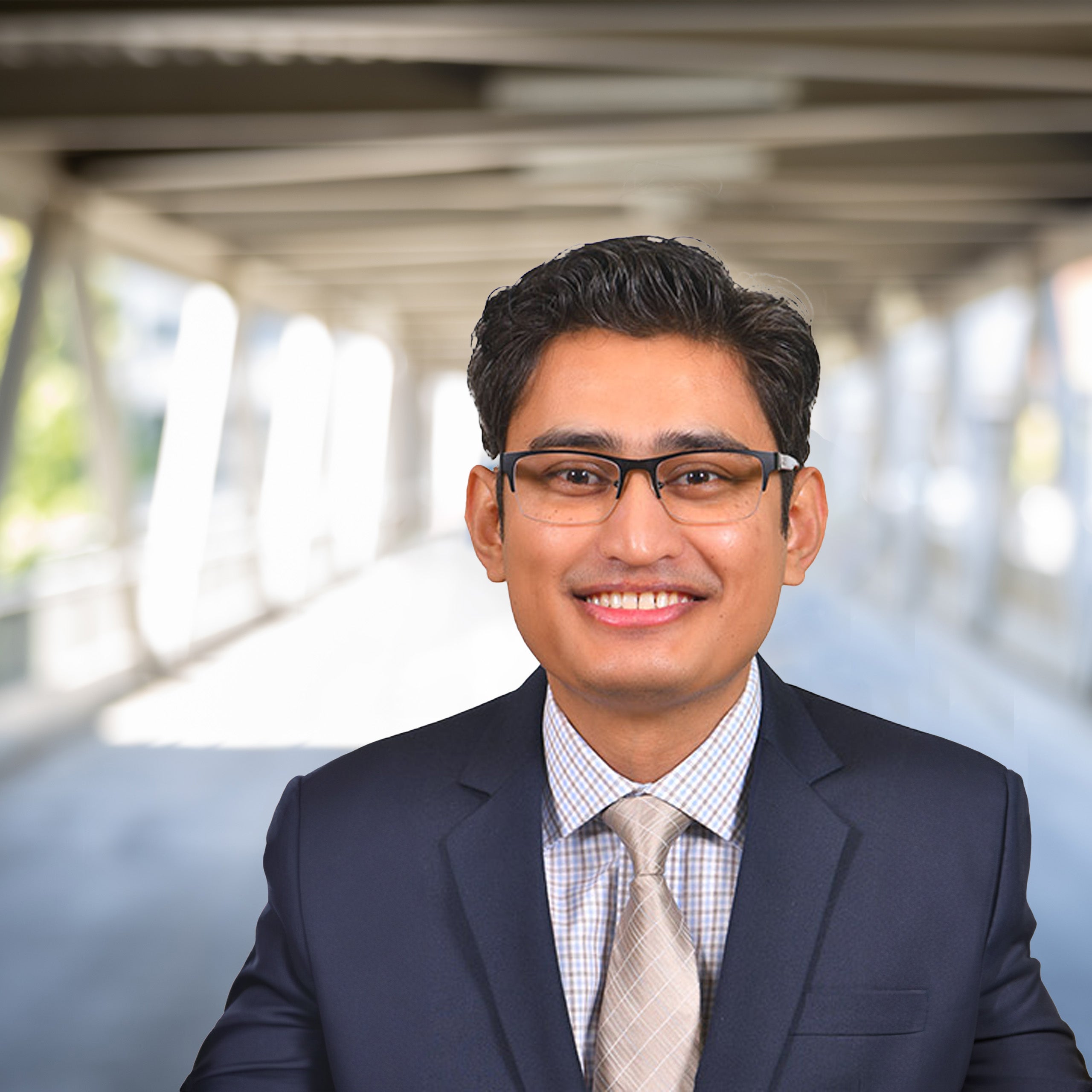Norman Khan headshot. Male with brown hair and eyes with glasses. He is wearing a suit.