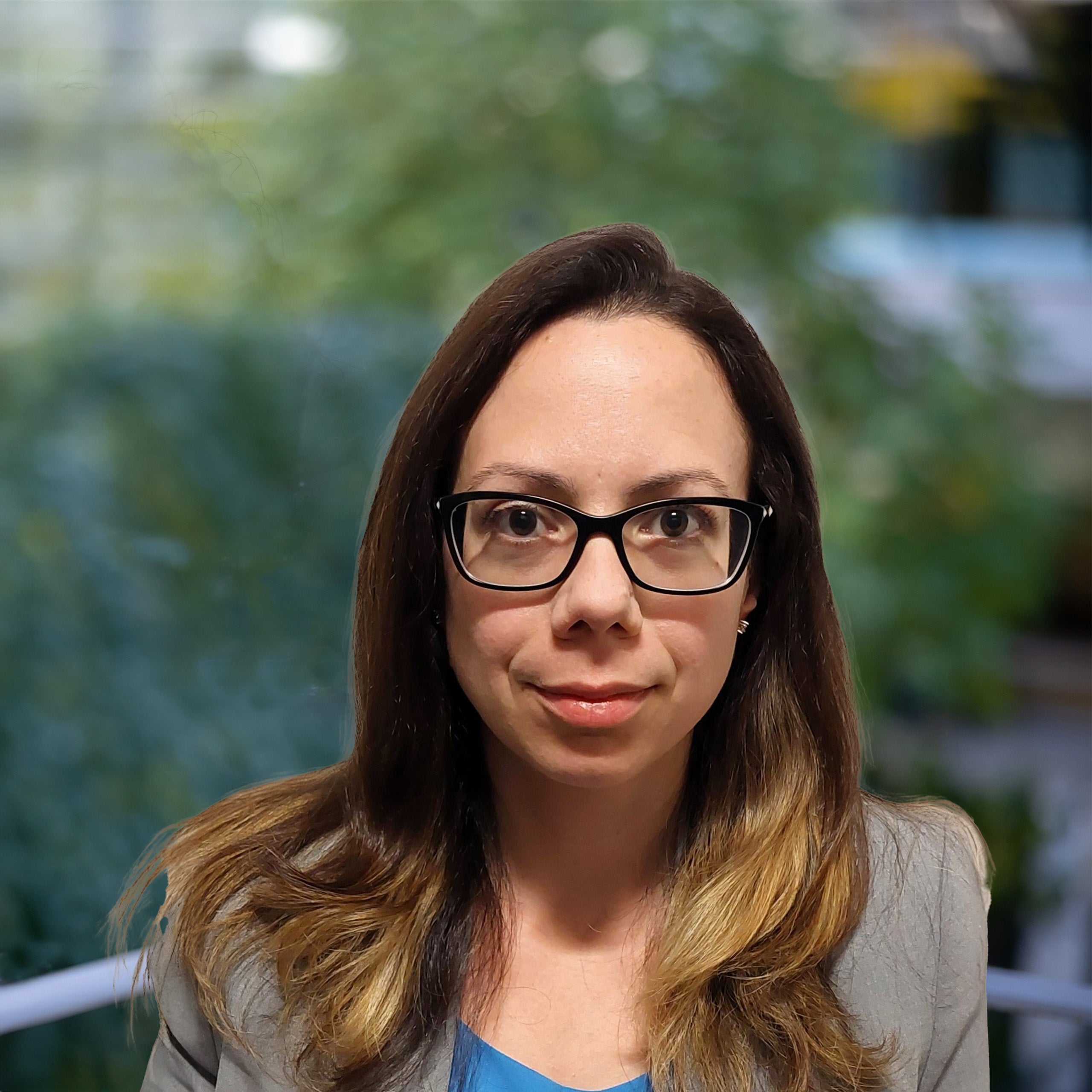 Virginie Papasoulou, PhD, headshot. A woman with long, honey-brown hair and brown eyes, wearing glasses, looks directly at the camera. She is wearing a blue blouse and a light grey jacket.