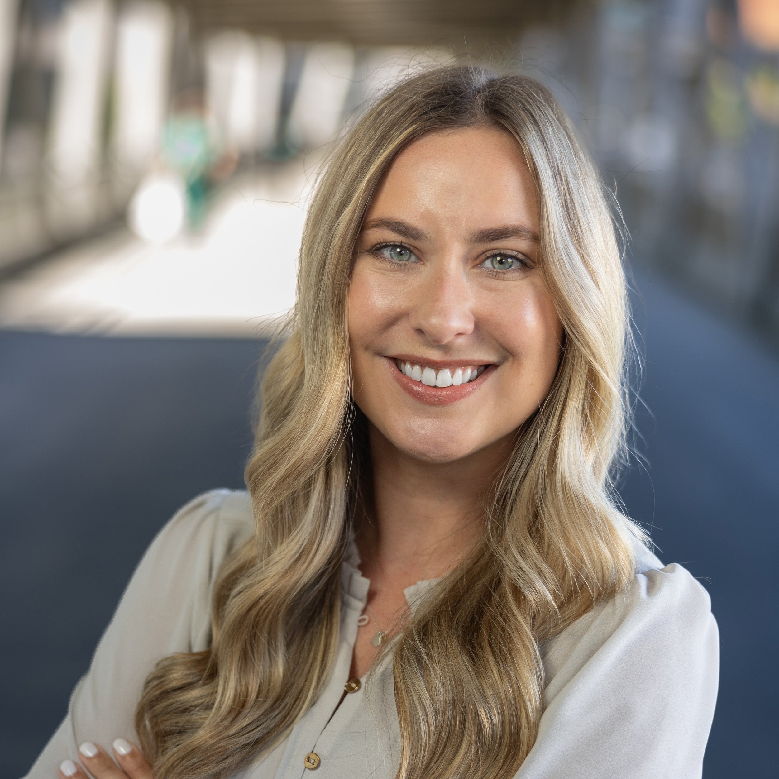 Candler Blake, MD, headshot. A young female with long blond hair and green eyes smiling at the camera in a cream long-sleeve blouse.