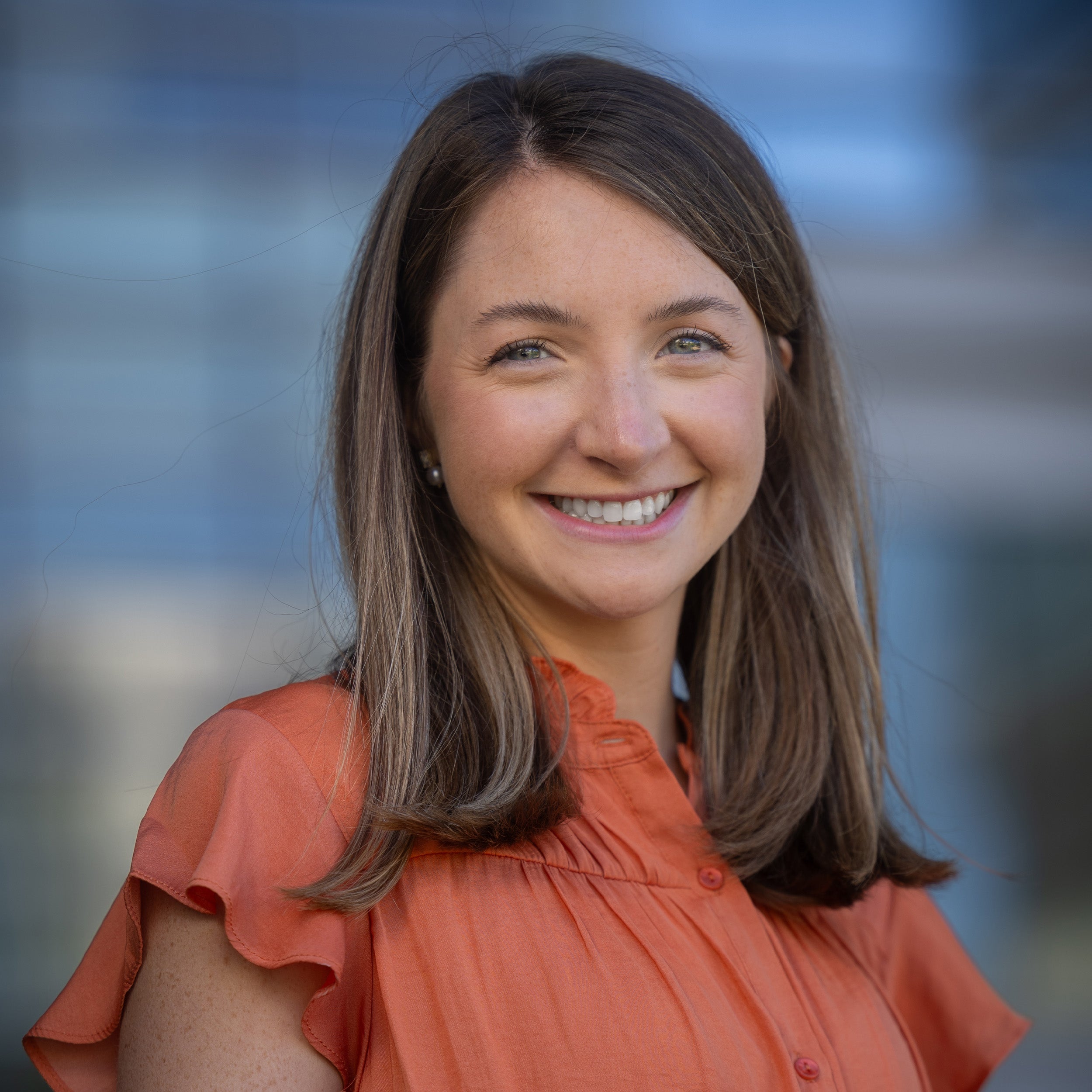 Caroline Day, MD, headshot. A young white female with long brown hair and blue eyes is smiling at the camera. She is wearing a coral blouse.