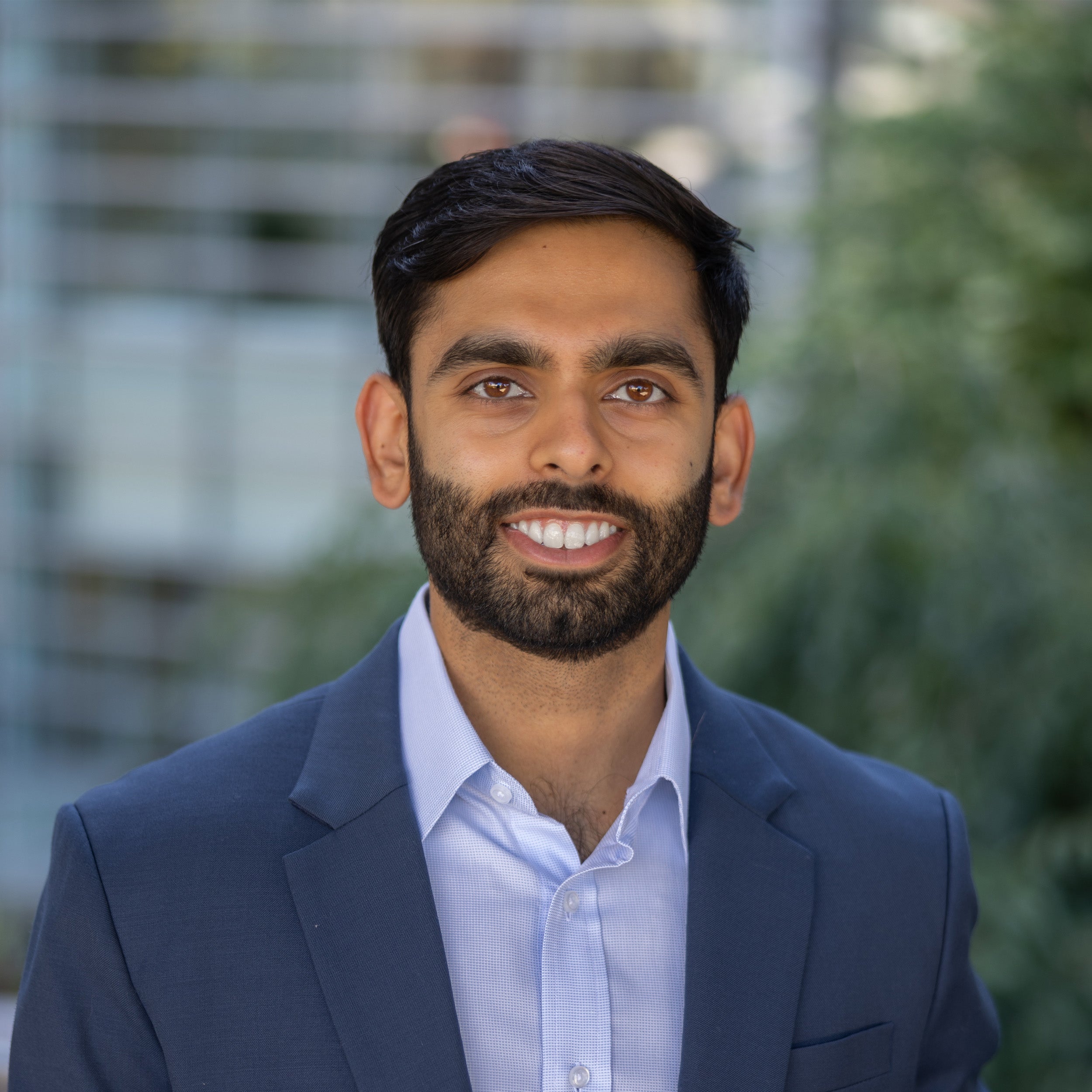 Vedang Patel, MD, headshot. Indian male with black hair, a beard, and brown eyes smiling at the camera. He is wearing a collard blue button-down shirt with a dark blue suit jacket.